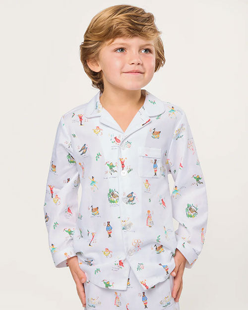 Child wearing a white pajama set featuring a long-sleeved, collared button-up shirt and matching pants, both adorned with colorful illustrations of animals, people, and nature scenes, standing against a plain background.