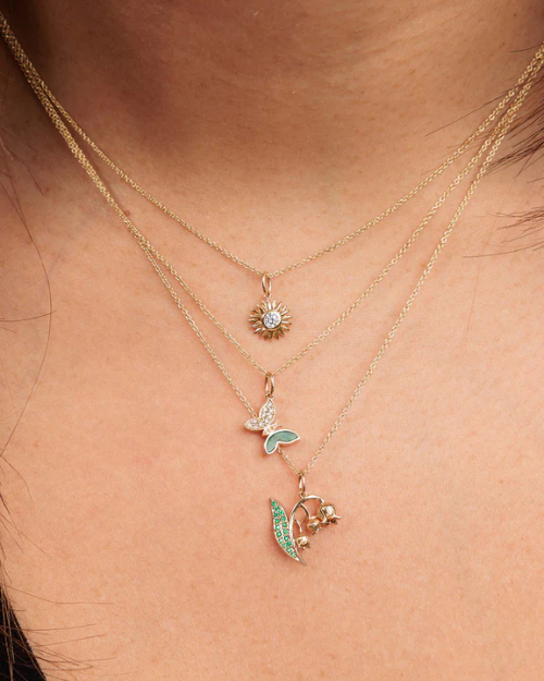 Close-up of a person wearing gold necklaces with flower and butterfly pendants.