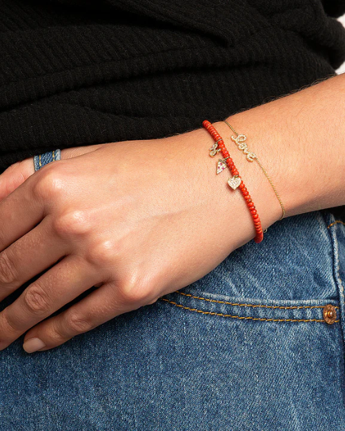 Close-up of a hand wearing a gold bracelet love script on a black sweater and blue jeans background.