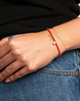 Close-up of a hand wearing a gold bracelet love script on a black sweater and blue jeans background.