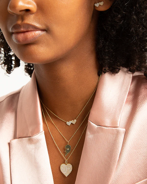 Close-up of a person wearing multiple necklaces with heart-shaped pendants.