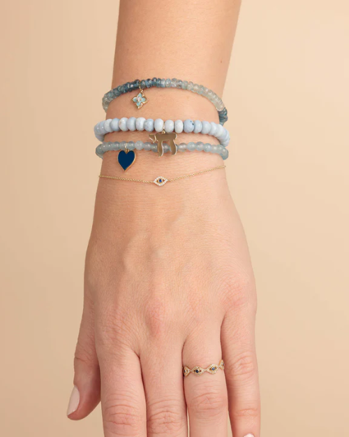 Hand wearing multiple blue bracelets on a beige background