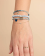 Hand wearing multiple blue bracelets on a beige background