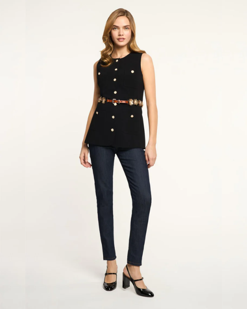 Woman wearing a black sleeveless top with gold buttons and navy pants on a white background