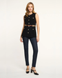 Woman wearing a black sleeveless top with gold buttons and navy pants on a white background