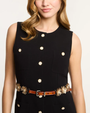 Black sleeveless dress with gold buttons and a brown belt worn by a model on a white background