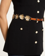 Black top with gold buttons and a decorative belt on a neutral background