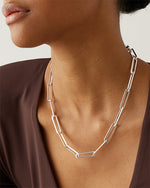 Close-up of model wearing silver chain necklace. Features large links resembling paperclips.