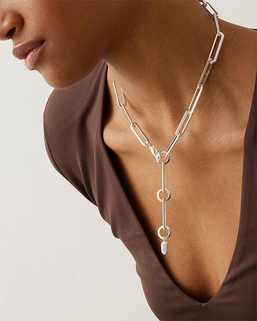 Close-up of model wearing silver chain necklace backwards, showcasing adjustable circular clasp closure. 