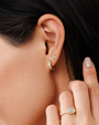 Close-up of an ear with a diamond butterfly earring and a hand wearing a ring with a yellow gemstone.