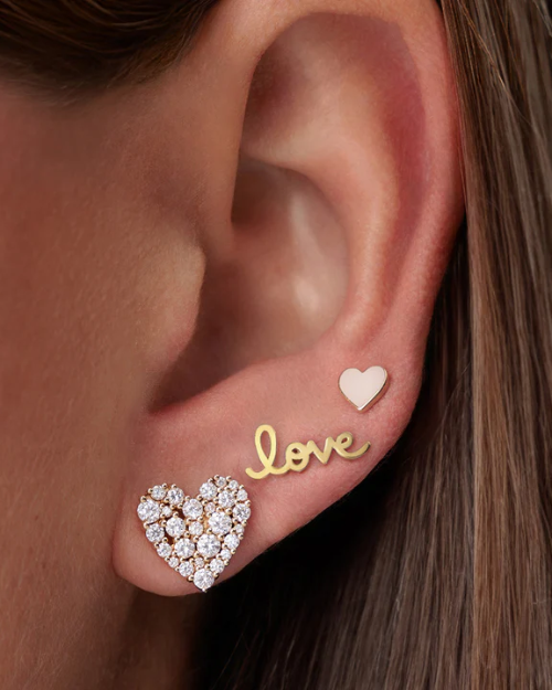 Close-up of an ear wearing gold 'love' and heart-shaped earrings.