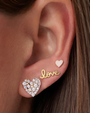 Close-up of an ear wearing gold 'love' and heart-shaped earrings.