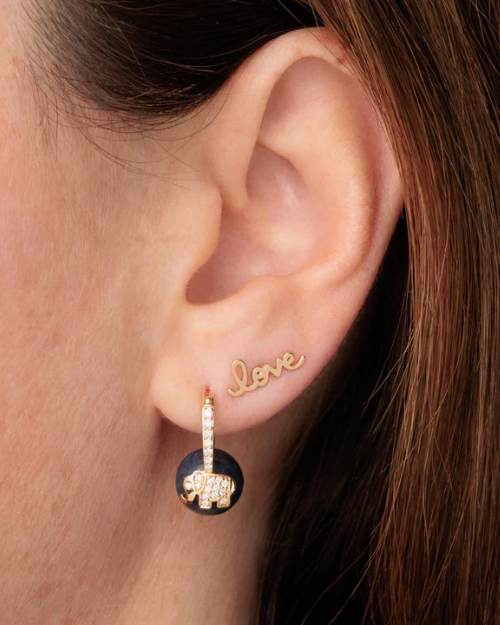 Close-up of an ear wearing gold 'love' earrings with a black and gold elephant earring.