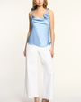 Woman wearing a light blue top and white pants on a plain background