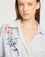 Woman wearing a light blue striped shirt with decorative embellishments.