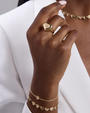 Hand wearing a gold heart-shaped ring with matching bracelet on a white background