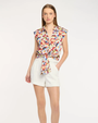 Woman wearing a colorful floral sleeveless top and white shorts on a light gray background