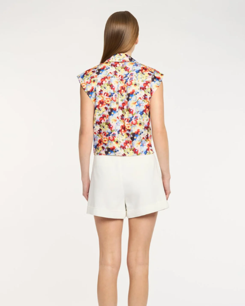 Woman wearing a colorful sleeveless top and white shorts on a plain background