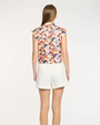 Woman wearing a colorful sleeveless top and white shorts on a plain background