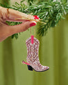 A hand holding a festive pink cowboy boot ornament featuring crystal accents, ideal for adding charm to a Christmas tree.