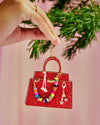  A hand grasps a red bag ornament shaped like a purse, suspended from a decorated Christmas tree.