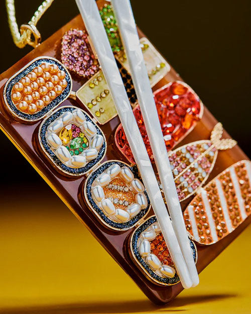 A decorative ornament of a plate of assorted sushi rolls with a pair of chopsticks resting beside it.