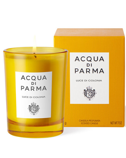 Acqua Parma orange candle displayed in a glass holder, emitting a warm glow against a neutral background.