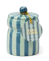 A blue and light green striped candle featuring a label, set against a neutral background.