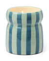 A blue and light green striped candle featuring a label, set against a neutral background.