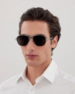 A man wearing a white shirt and sunglasses stands confidently, showcasing a casual yet stylish appearance.