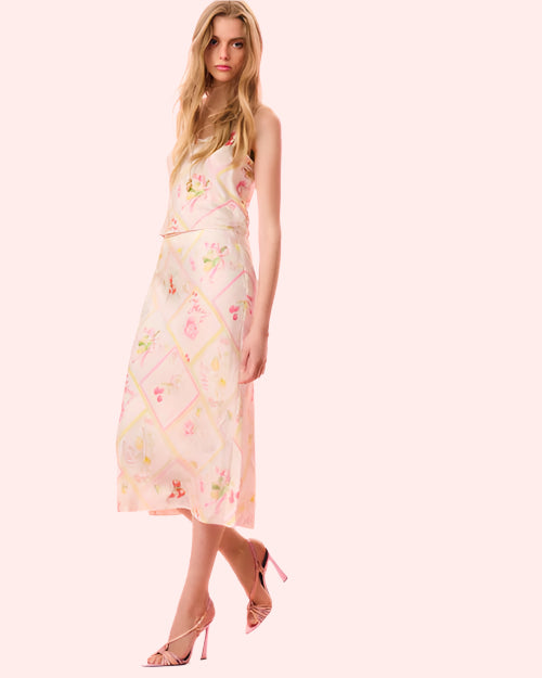 A model poses in a pink and white floral top and skirt, showcasing a vibrant floral pattern against a soft background.
