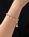 A zoomed in photo of a models wrist wearing a two-toned, half silver and gold bracelet with round beads evenly spaced around it, and a dangling sphere charm.