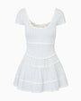 A dress in front of a white background, featuring a pattern of thin blue and white stripes, with a low rounded neckline and lace ring detailing on the lightly ruffled skirt and hems. 