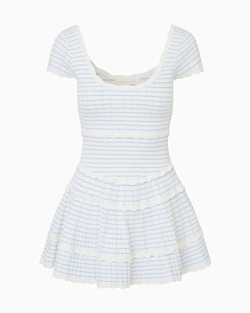 A dress in front of a white background, featuring a pattern of thin blue and white stripes, with a low rounded neckline and lace ring detailing on the lightly ruffled skirt and hems. 
