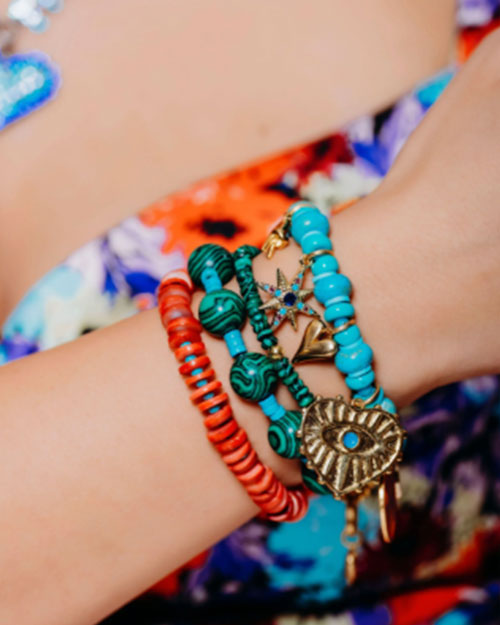 A close-up of a person's wrist adorned with multiple bracelets. The bracelets are colorful and varied in design, including red, turquoise, and green beads. 