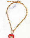 A close-up of a gold chain necklace in front of a marble background. The necklace features a starburst design in the center made of small white crystals. The chain is linked to the pendant through a circular ring that is also adorned with small white crystals. 