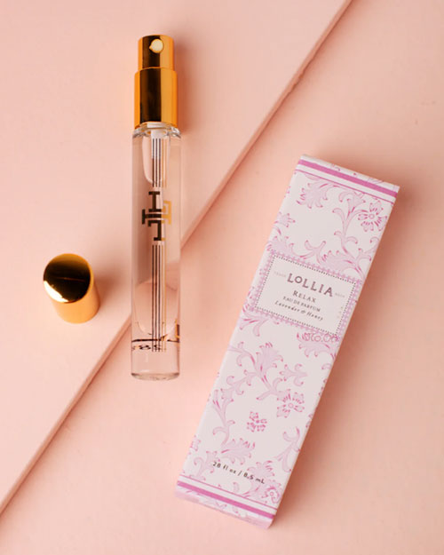 An overhead view of a perfume bottle adorned with elegant gold accents and an opened cap, lying next to a white and pink florally designed box with the label "LOLLIA" in the center and "no22" at the top.