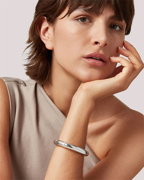 A woman dressed in beige, showcasing a silver bracelet on her wrist, exuding grace and style.

