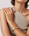 A woman dressed in beige, showcasing a silver bracelet on her wrist, exuding grace and style.