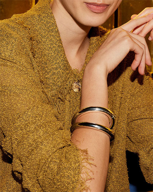 A woman dressed in a sweater and adorned with a silver bracelet, exuding a warm and cheerful demeanor.