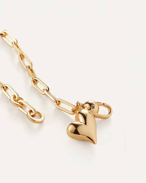 A gold heart charm attached to a delicate chain bracelet, showcasing a simple yet elegant design.