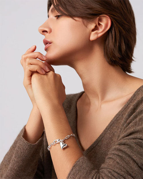 A woman dressed in a brown sweater, showcasing a silver bracelet on her wrist, with a gentle expression.