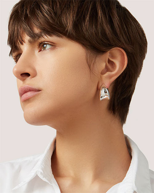 A woman wearing a white shirt and wearing a silver earring featuring a stylish curved design, looking directly at the camera with a friendly expression.  