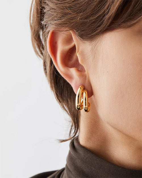 A pair of gold metal hoop earrings, featuring a classic design with a polished finish, set on a simple backdrop.