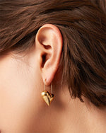 A woman adorned with a gold heart-shaped earring, emphasizing her chic and sophisticated look