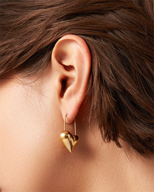 A woman adorned with a gold heart-shaped earring, emphasizing her chic and sophisticated look