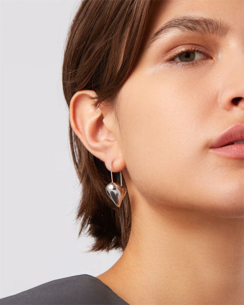  A woman wearing silver heart-shaped hoop earrings, showcasing a stylish and elegant accessory.

