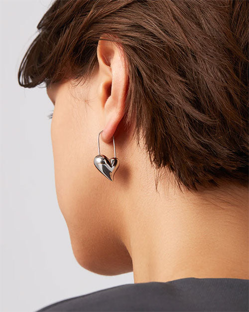 A woman wearing stylish silver hoop earrings shaped like hearts, showcasing a modern and elegant design.