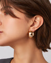 A woman is wearing a gold earring, showcasing its elegant design against her hairstyle.