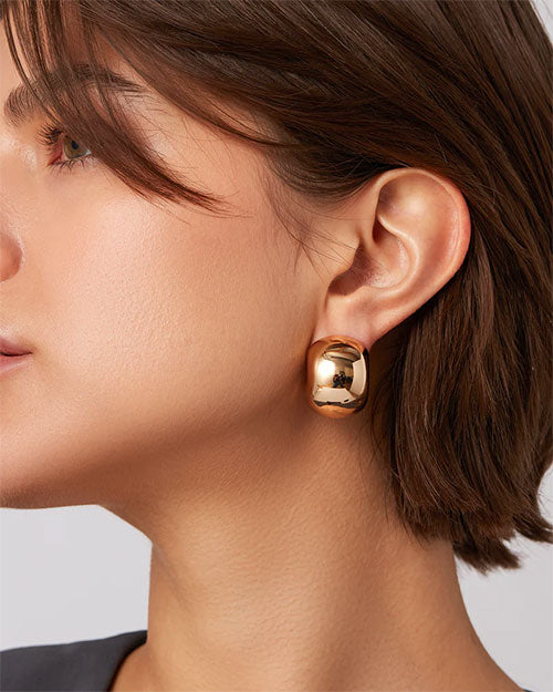 A woman is wearing a gold earring, showcasing its elegant design against her hairstyle.